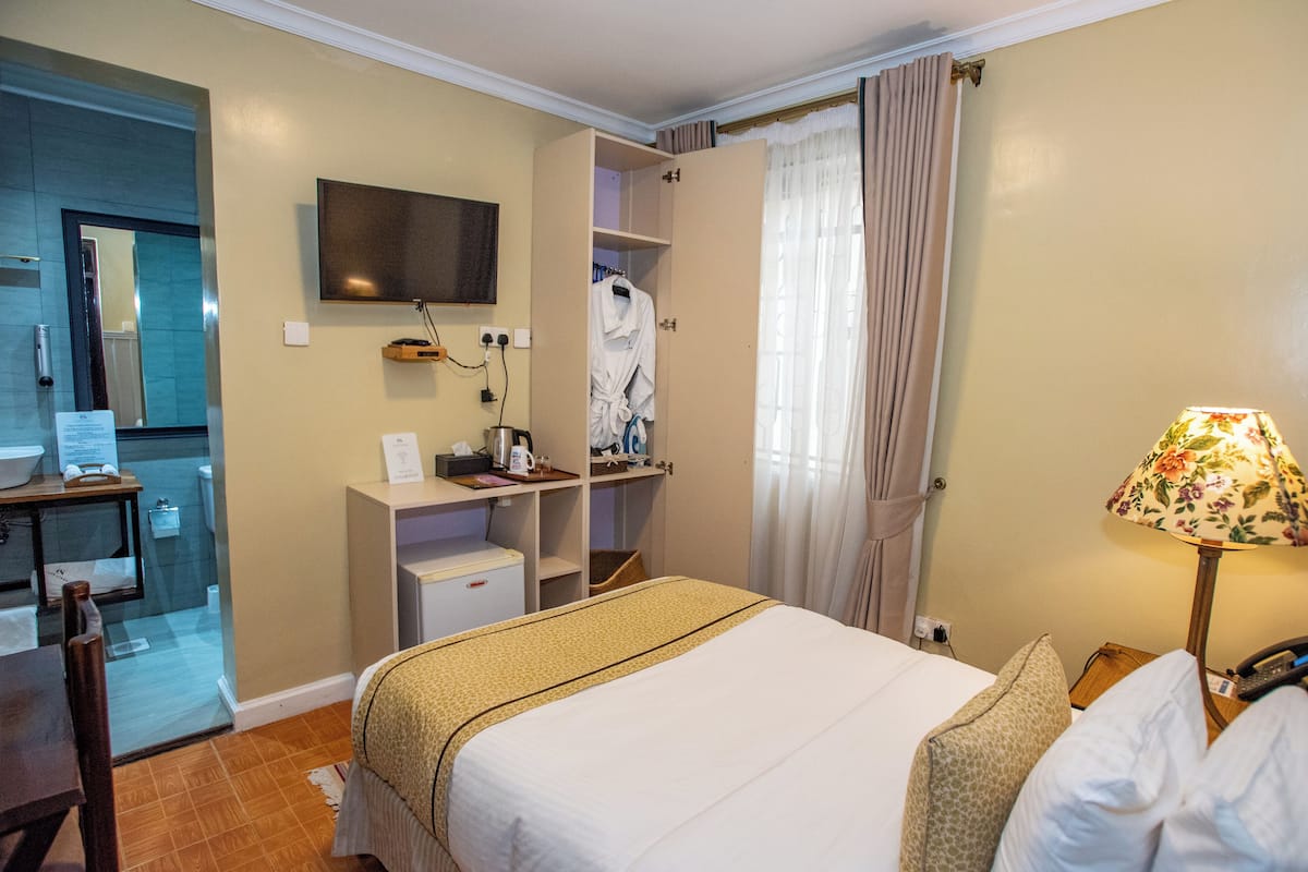 A hotel room with a bed, a desk with a computer, a TV, and a bathroom visible through an open door.