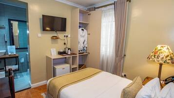 Habitación de hotel con cama, escritorio con computadora, televisión y baño visible a través de una puerta abierta.