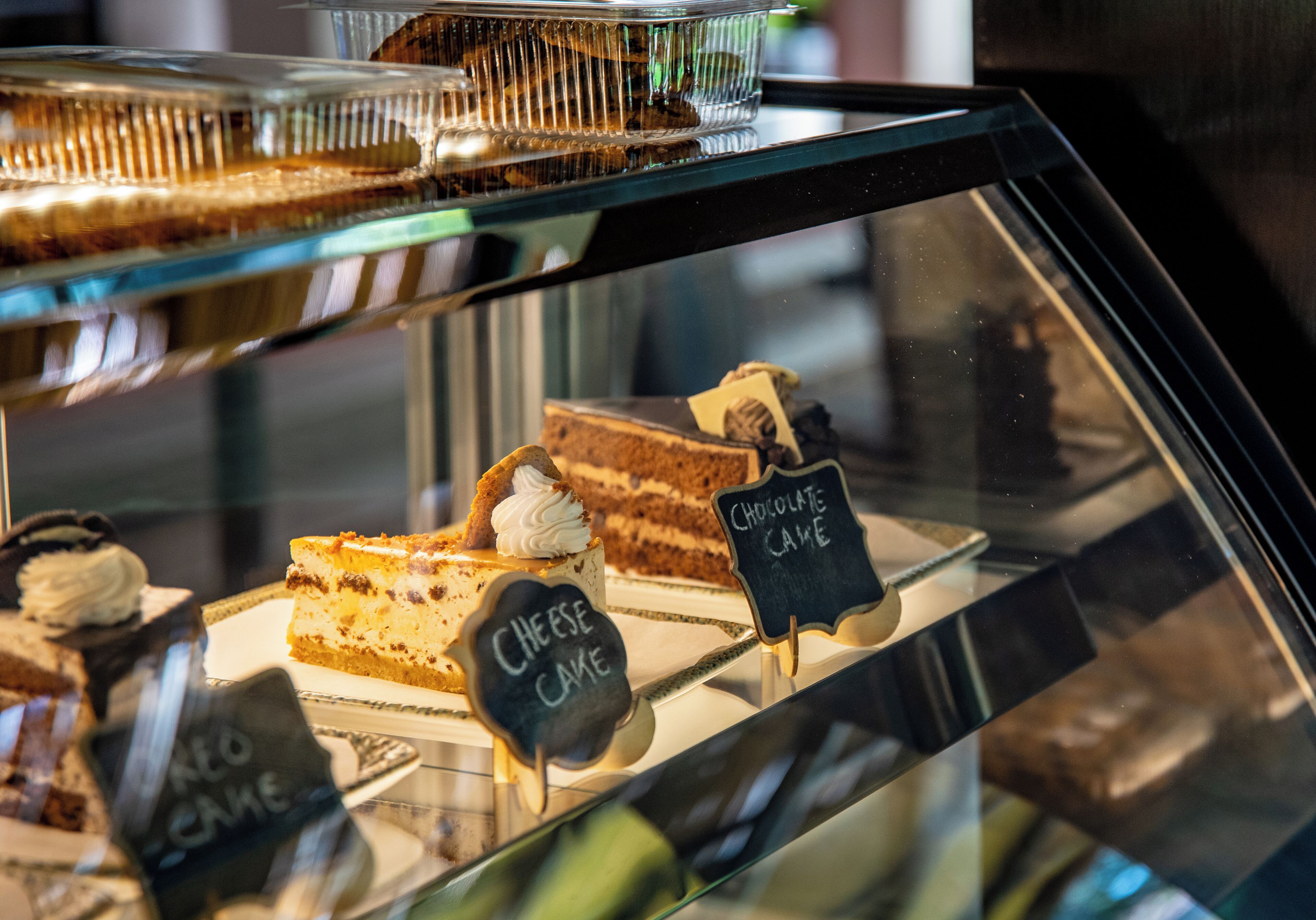 A display case with various cakes, including labeled sections for chocolate cake and cheese cake.