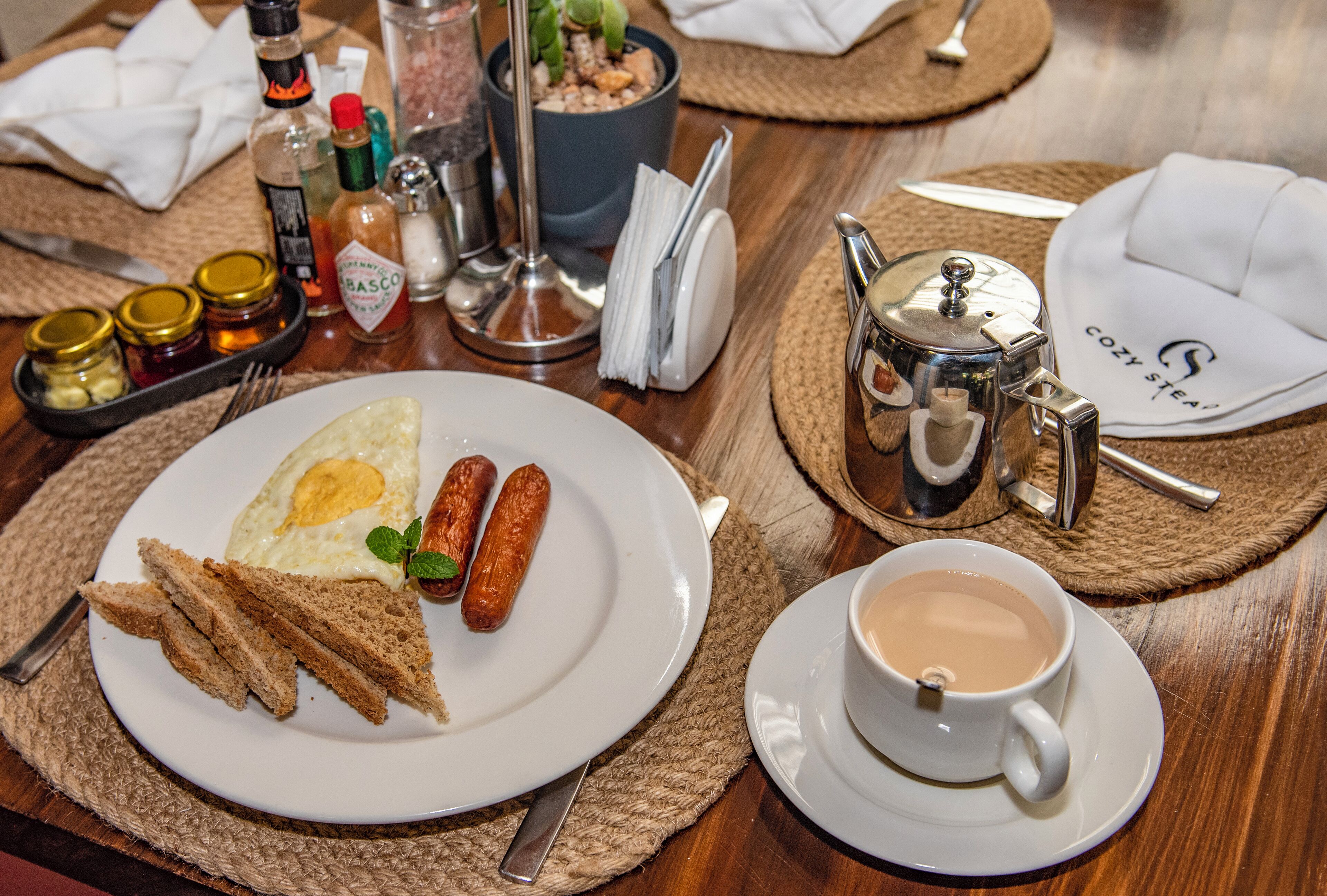 A breakfast setting with toast, sausages, a fried egg, and a cup of coffee on a wooden table.
