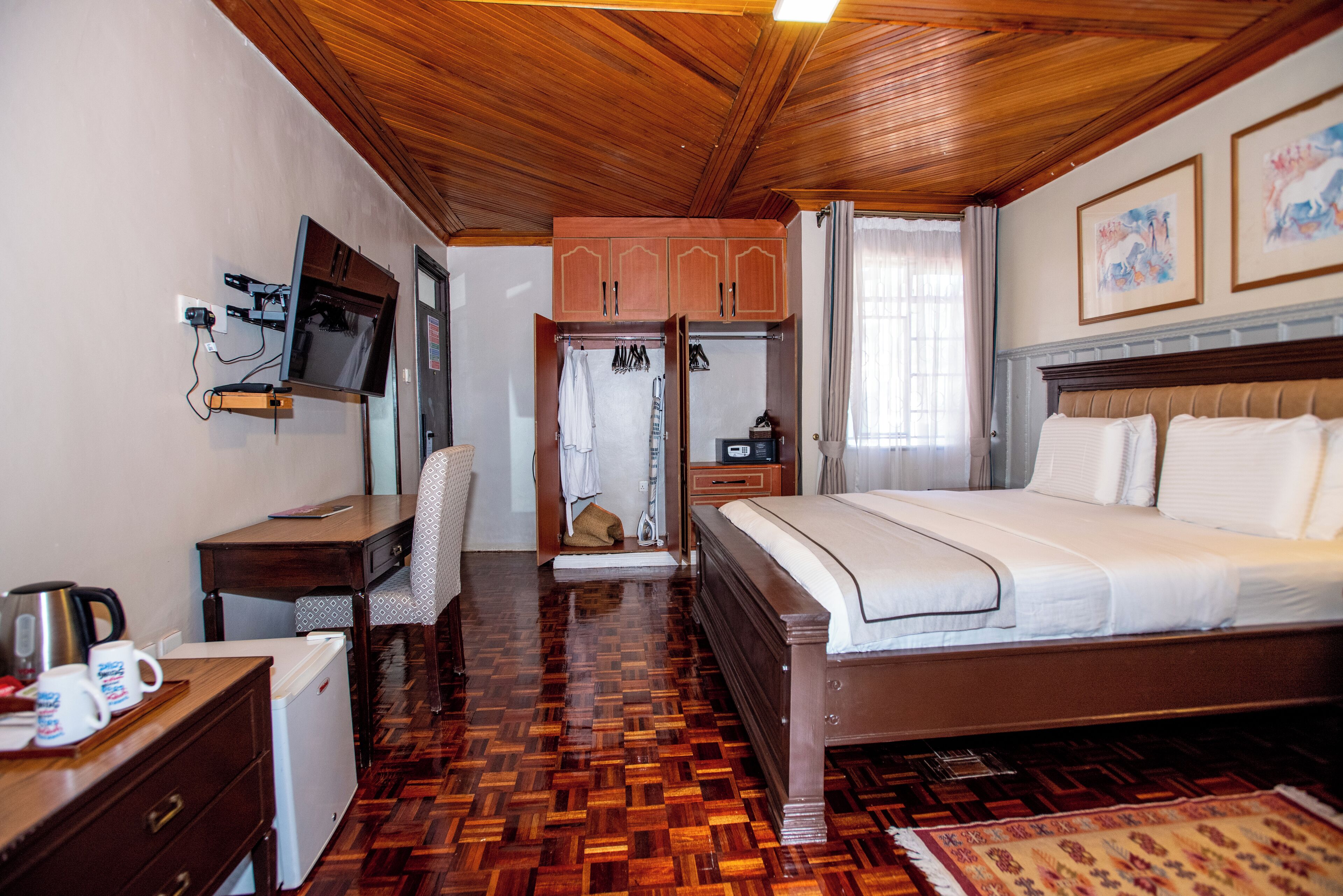 Habitación de hotel con techo de madera, una cama, un escritorio con televisor, un refrigerador pequeño y un armario.