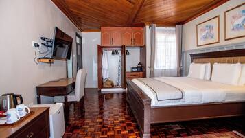 Habitación de hotel con techo de madera, una cama, un escritorio con televisor, un refrigerador pequeño y un armario.