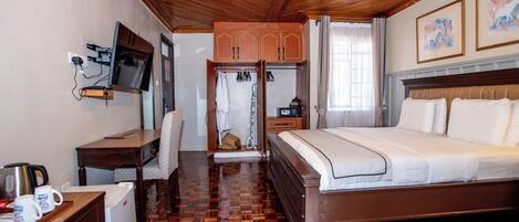 Habitación de hotel con techo de madera, una cama, un escritorio con televisor, un refrigerador pequeño y un armario.