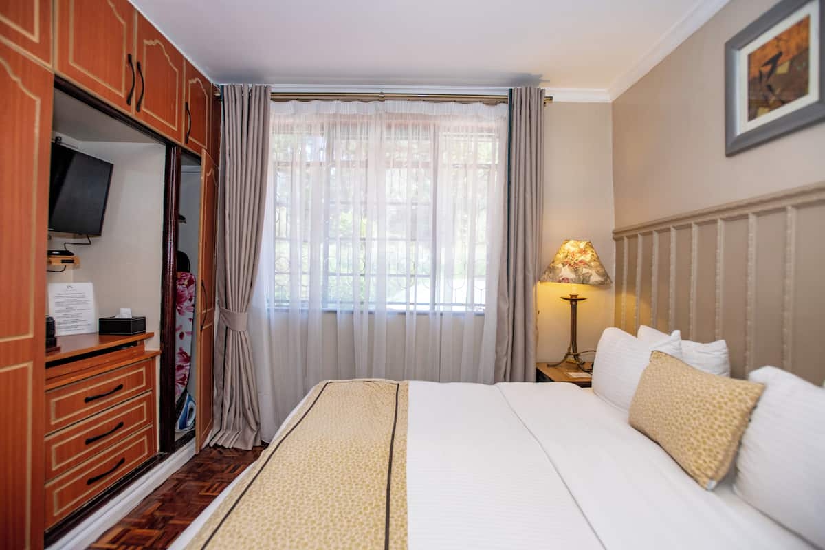 A hotel room with a bed, a television, a desk, and a window with curtains.