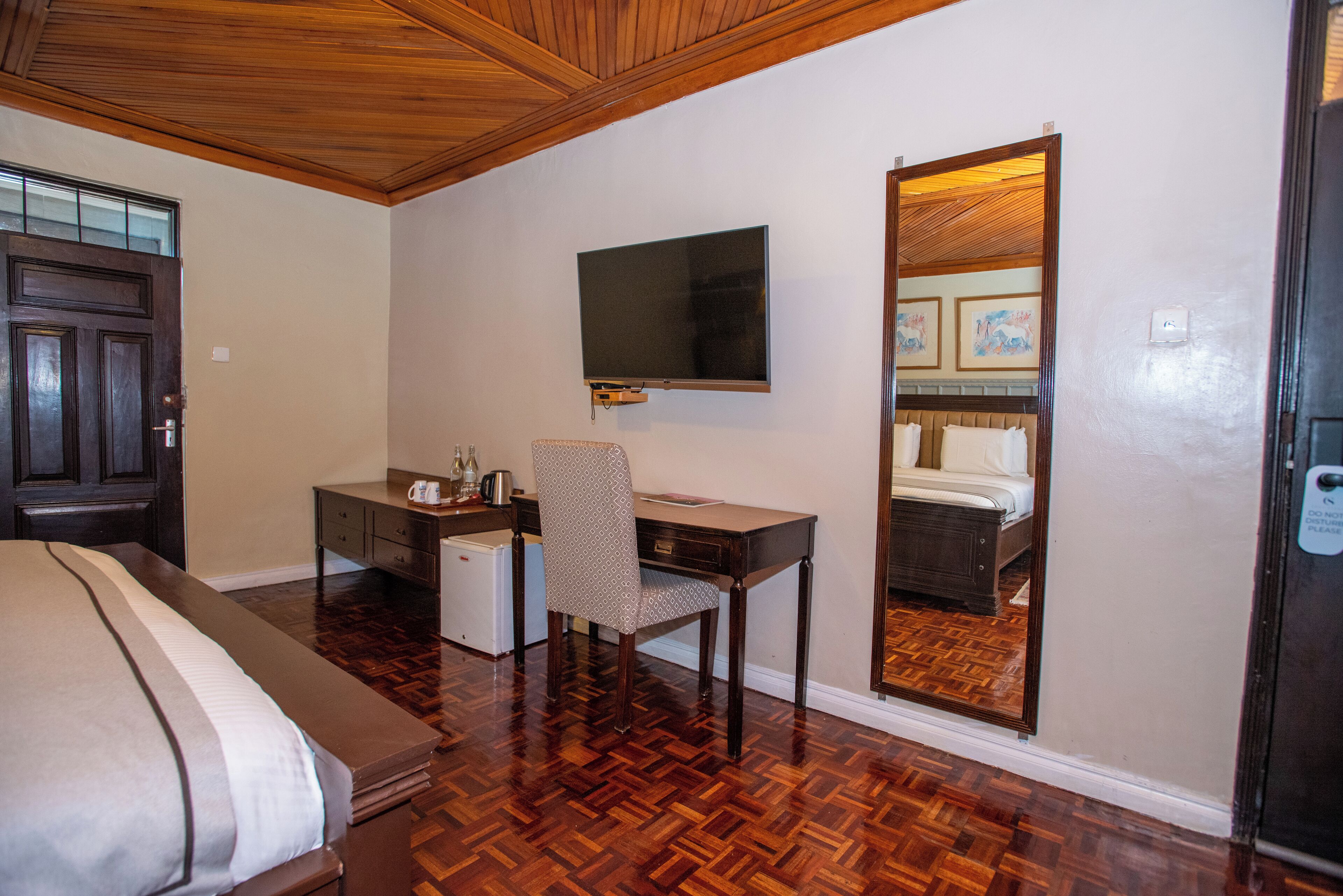 Habitación de hotel con cama, escritorio, silla, televisor y un espejo grande.