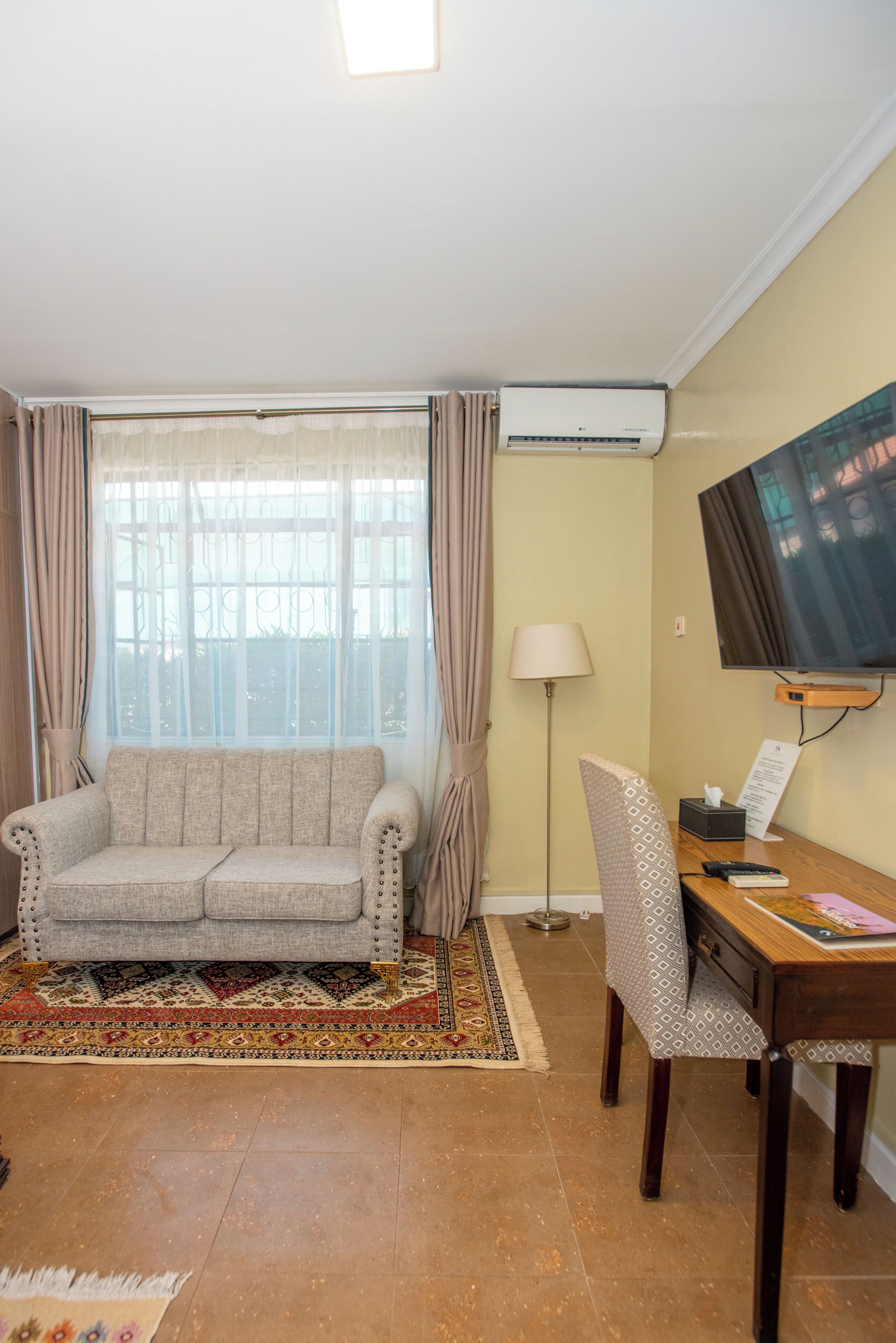 Un salon avec un canapé, un téléviseur, un bureau et une fenêtre avec des rideaux.