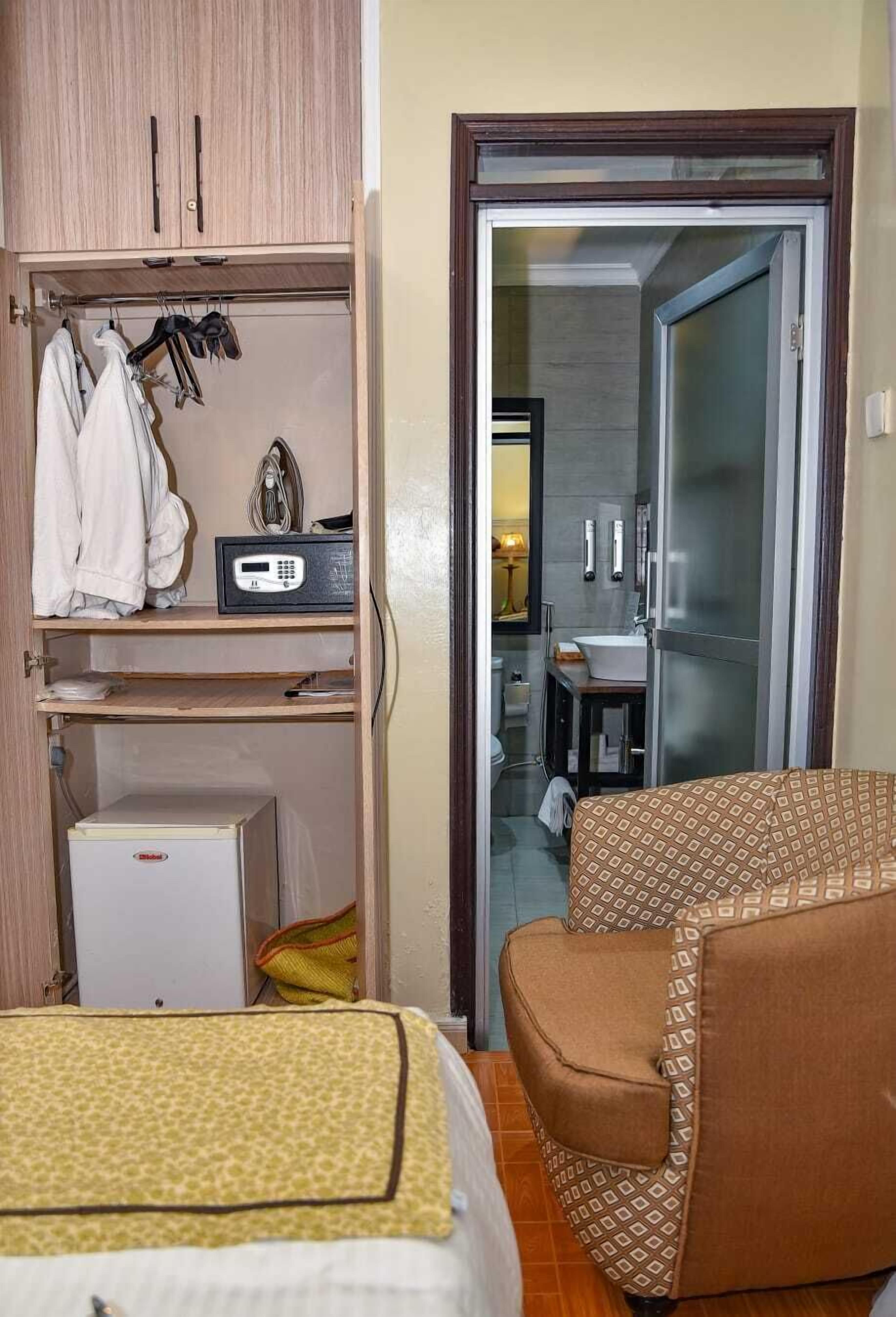 Habitación de hotel con armario, refrigerador pequeño, cama con manta estampada y sofá.