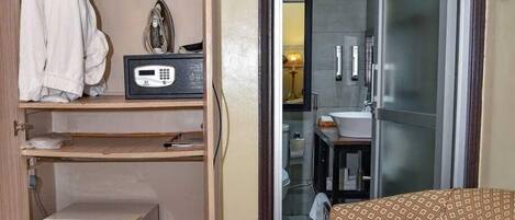 Habitación de hotel con armario, refrigerador pequeño, cama con manta estampada y sofá.