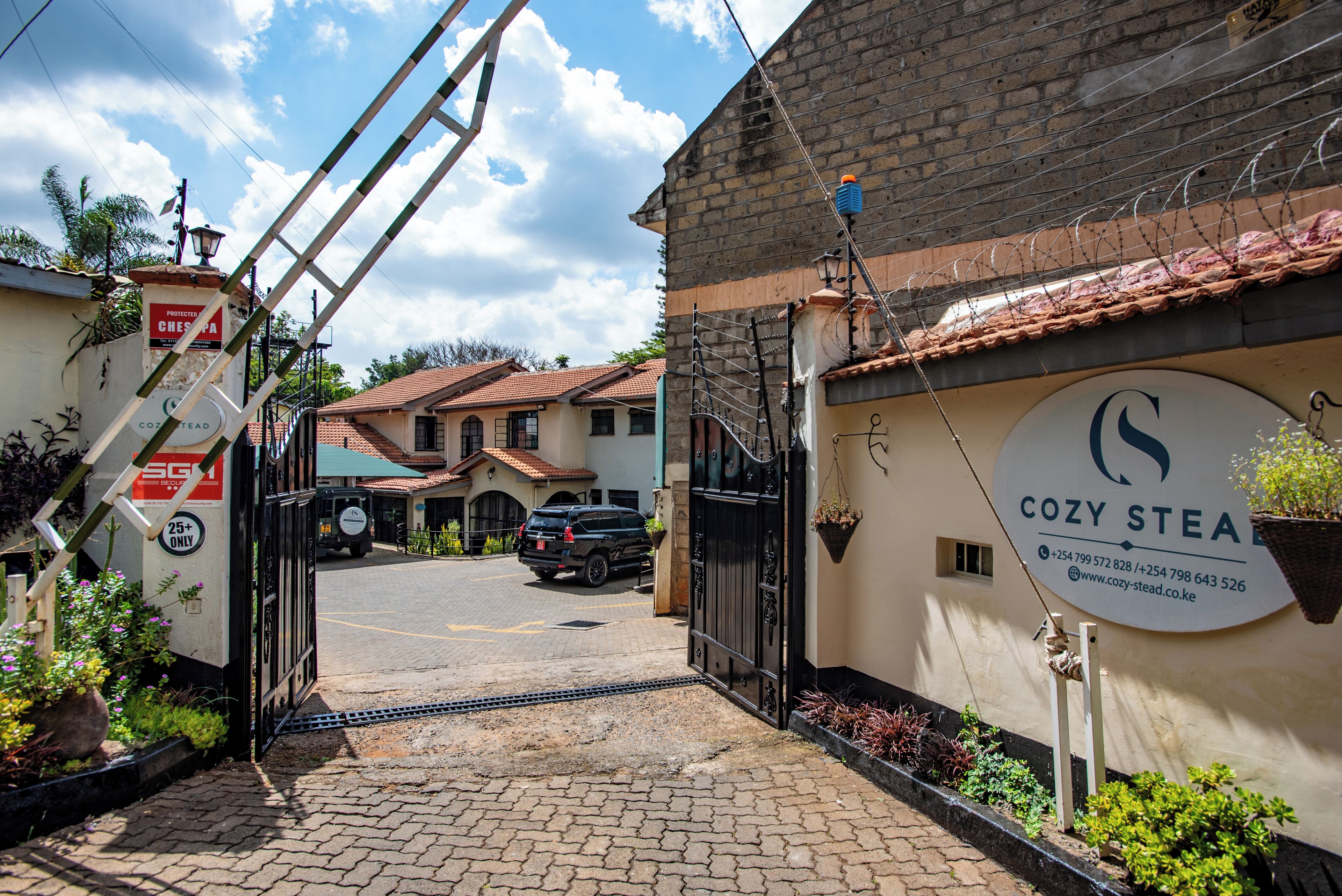 A gated entrance to a property with a sign reading "COZY STEAD" and contact information.