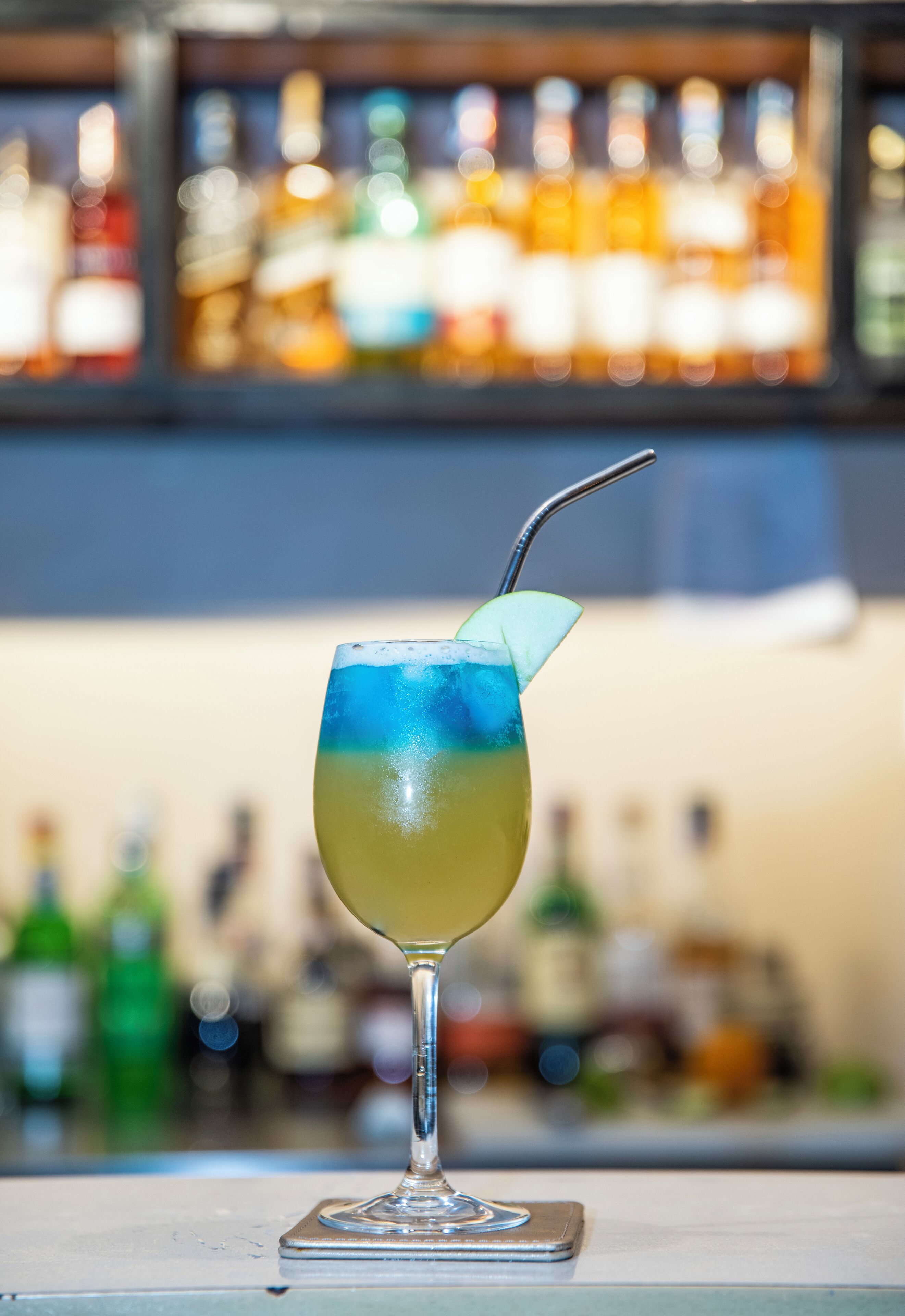 A cocktail glass with a straw and a lime slice on a bar counter.