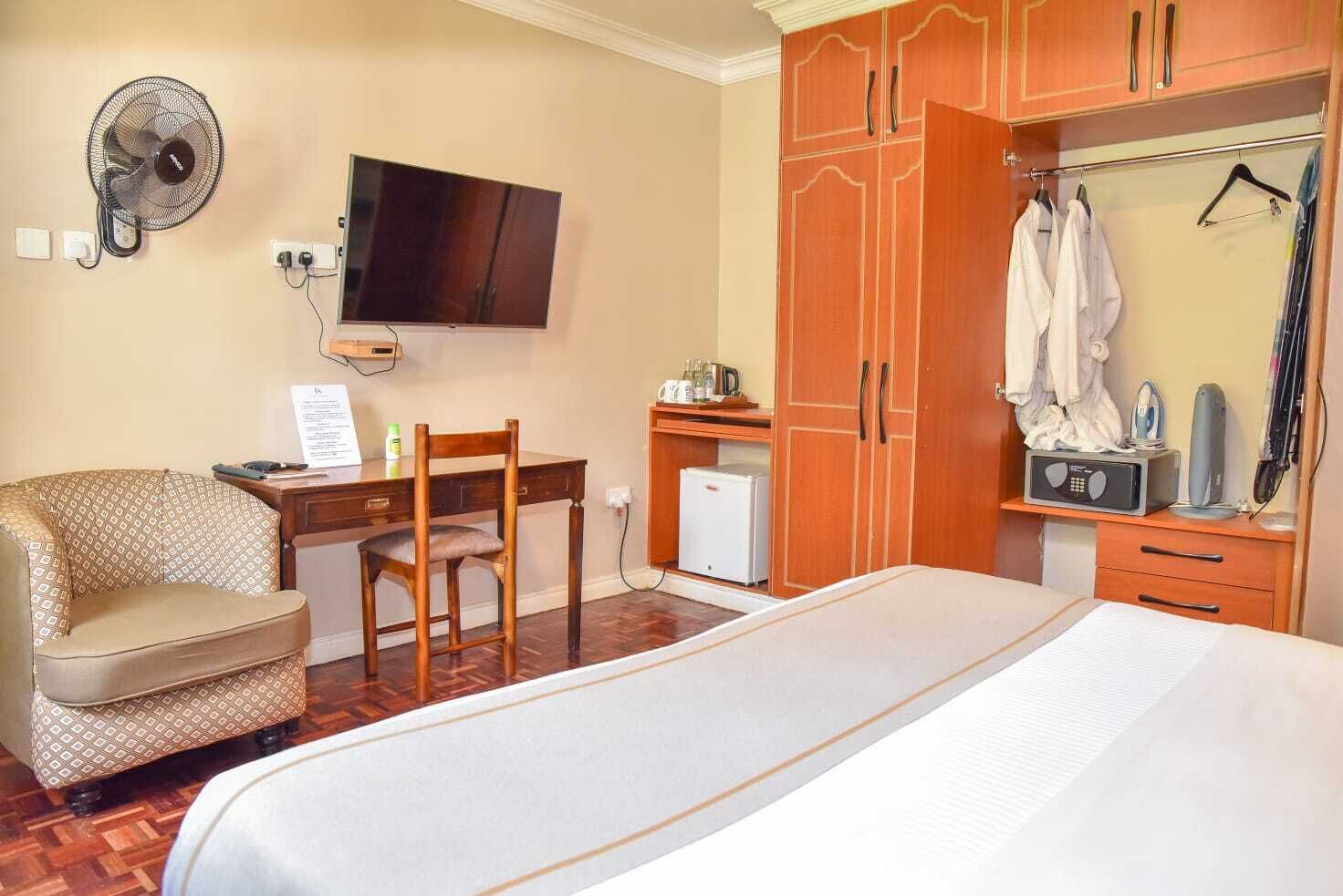 A hotel room with a bed, a desk, a chair, a television, a wardrobe, and a small refrigerator.