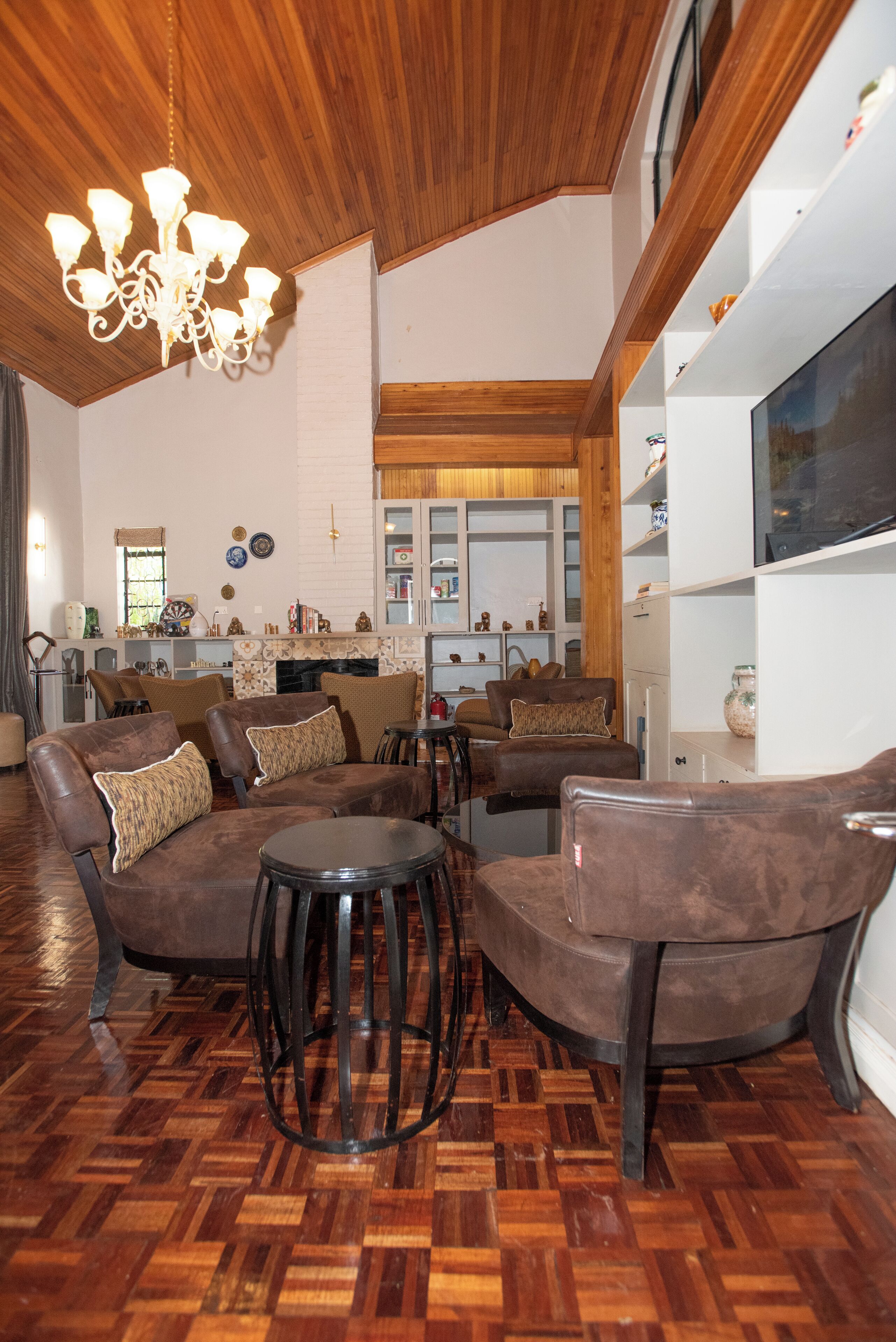 A spacious living room with a wooden ceiling, a chandelier, and leather sofas with cushions.
