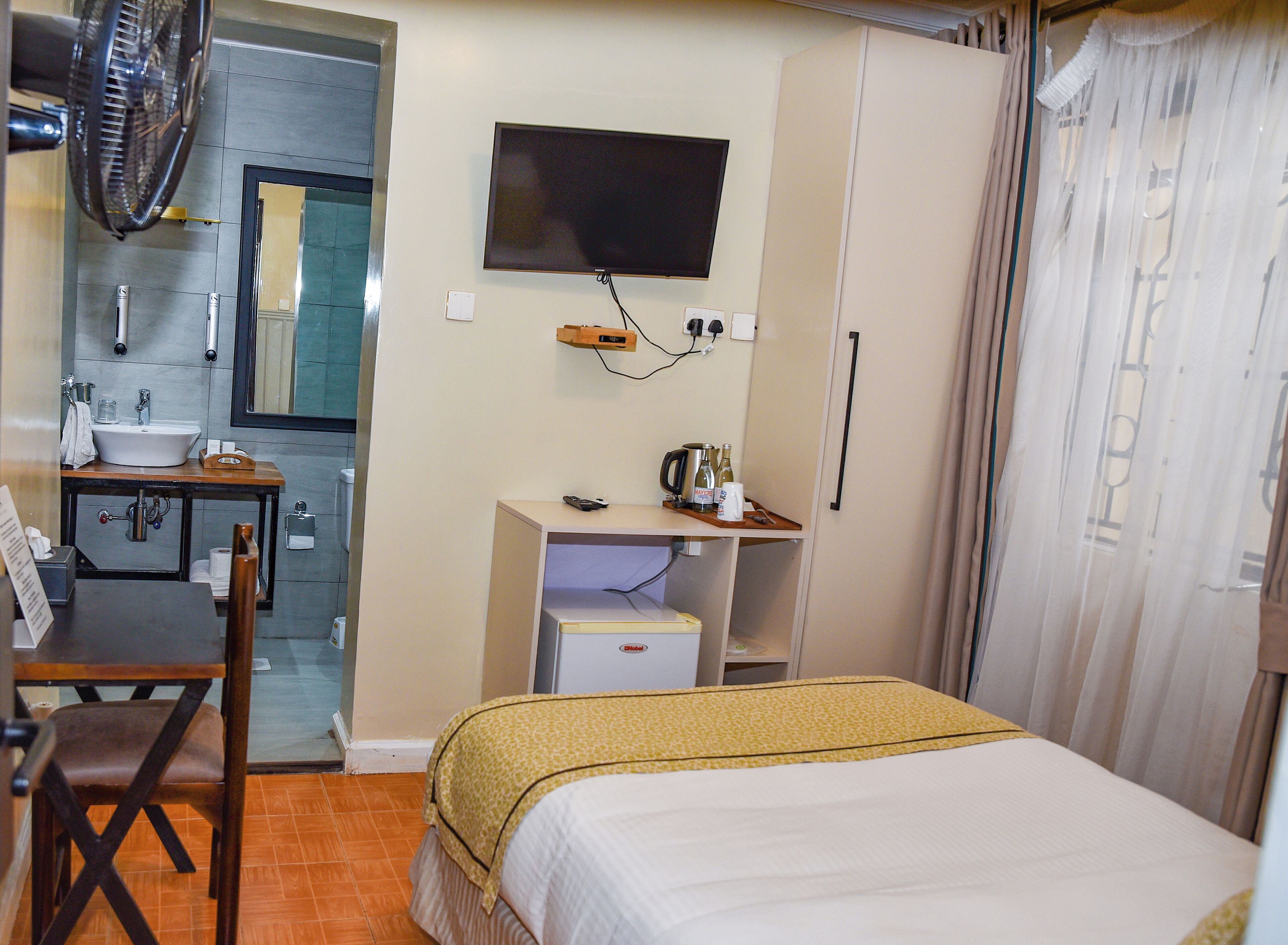 A hotel room with a bed, a desk with a computer, a television, a small kitchenette, and a bathroom.