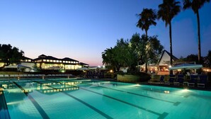 A hotel with a swimming pool, lounge chairs, and palm trees.
