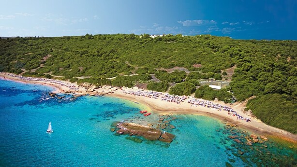 An aerial view of a coastal area with a beach, clear blue waters, and a sailboat.