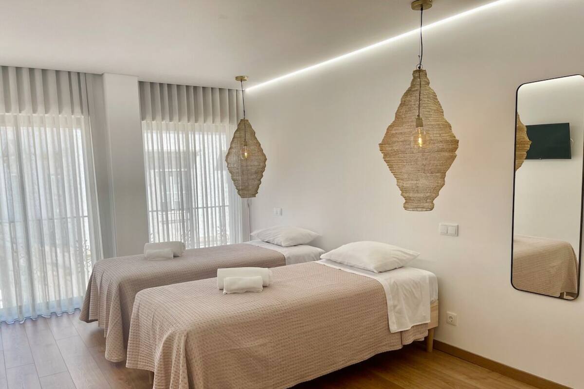 A hotel room with two beds, a large mirror, and a modern chandelier.