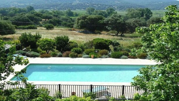 A rectangular pool with a white deck, surrounded by a black metal fence, set against a backdrop of lush greenery and distant hills. - Duplex 6 people in Corsica in residence with swimming pool (Serra-di-Ferro)