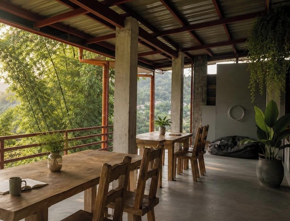 Une table à manger en bois, avec des chaises, une plante en pot et une vue sur la verdure.