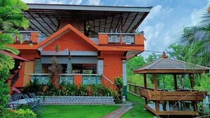 Una casa moderna con techo inclinado, un balcón con barandillas decorativas y un pequeño pabellón de madera en el jardín.