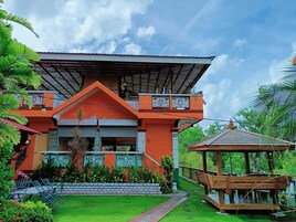Una casa moderna con techo inclinado, un balcón con barandillas decorativas y un pequeño pabellón de madera en el jardín.