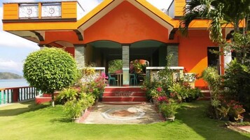 Un edificio colorido con una entrada acogedora, rodeado de exuberante vegetación y vistas al agua.