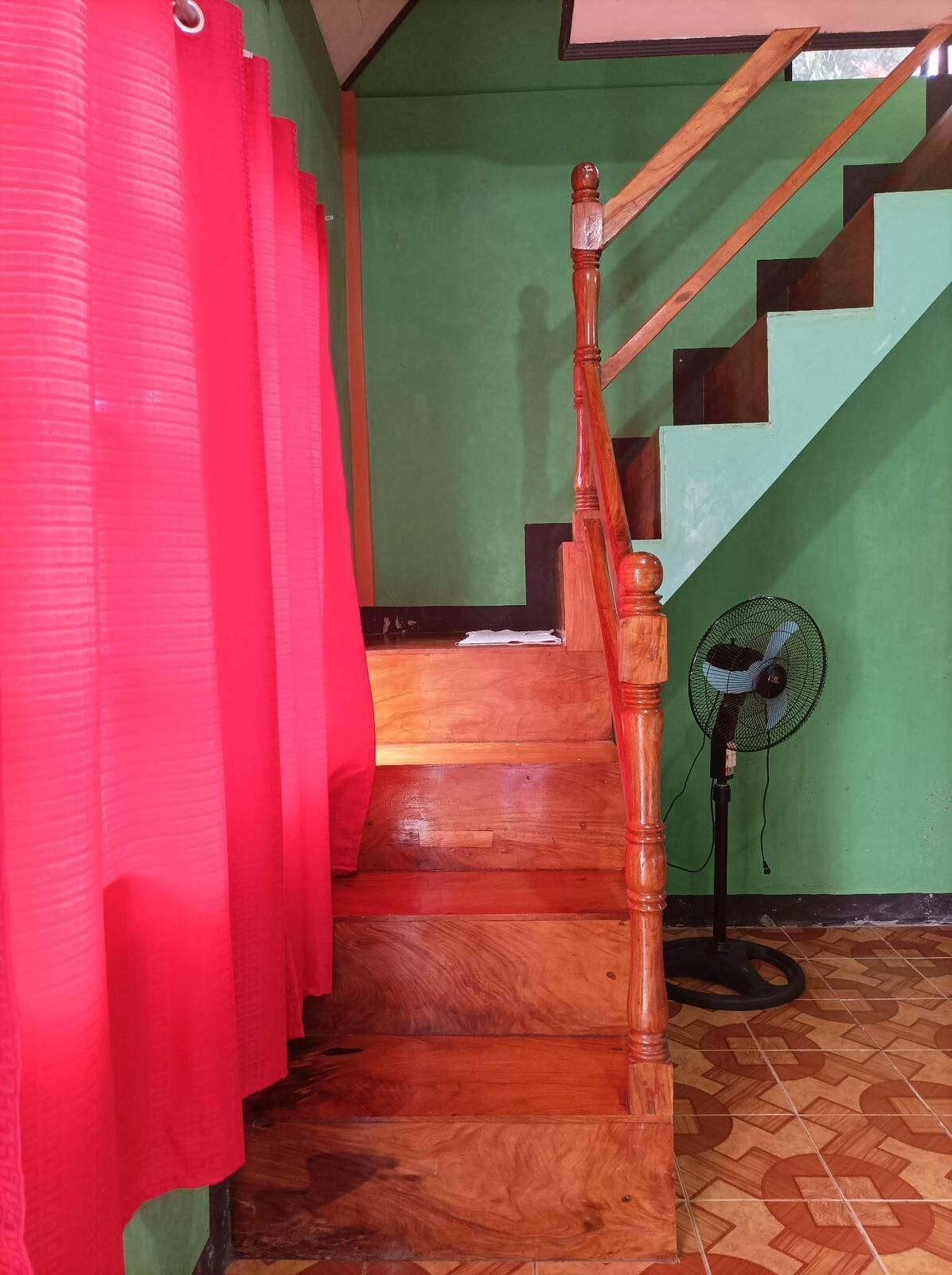 A wooden staircase with a handrail, a green wall, and a fan on the floor.