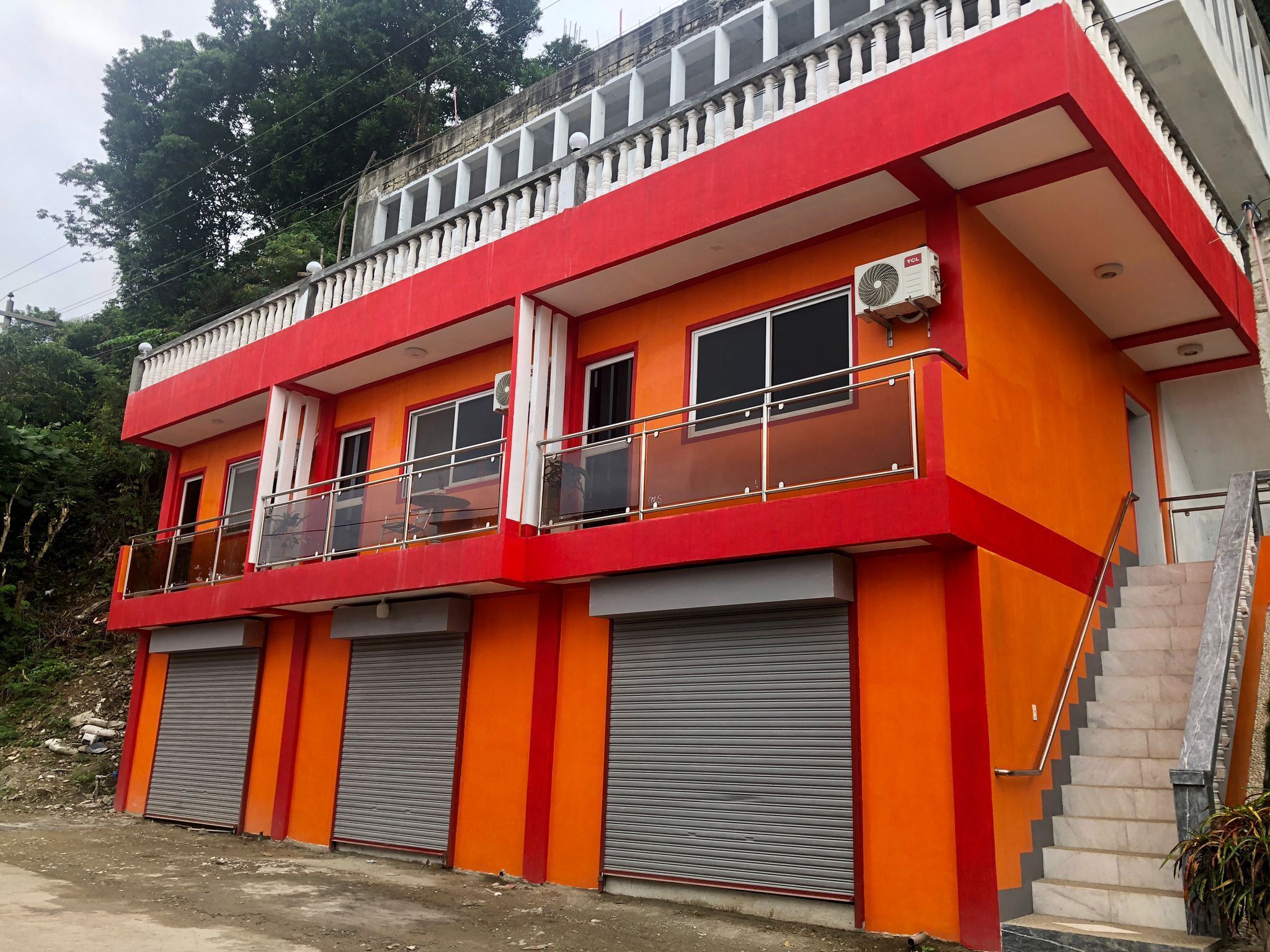 A multi-story building with a red and orange facade, balconies, and a staircase leading to the upper floor.