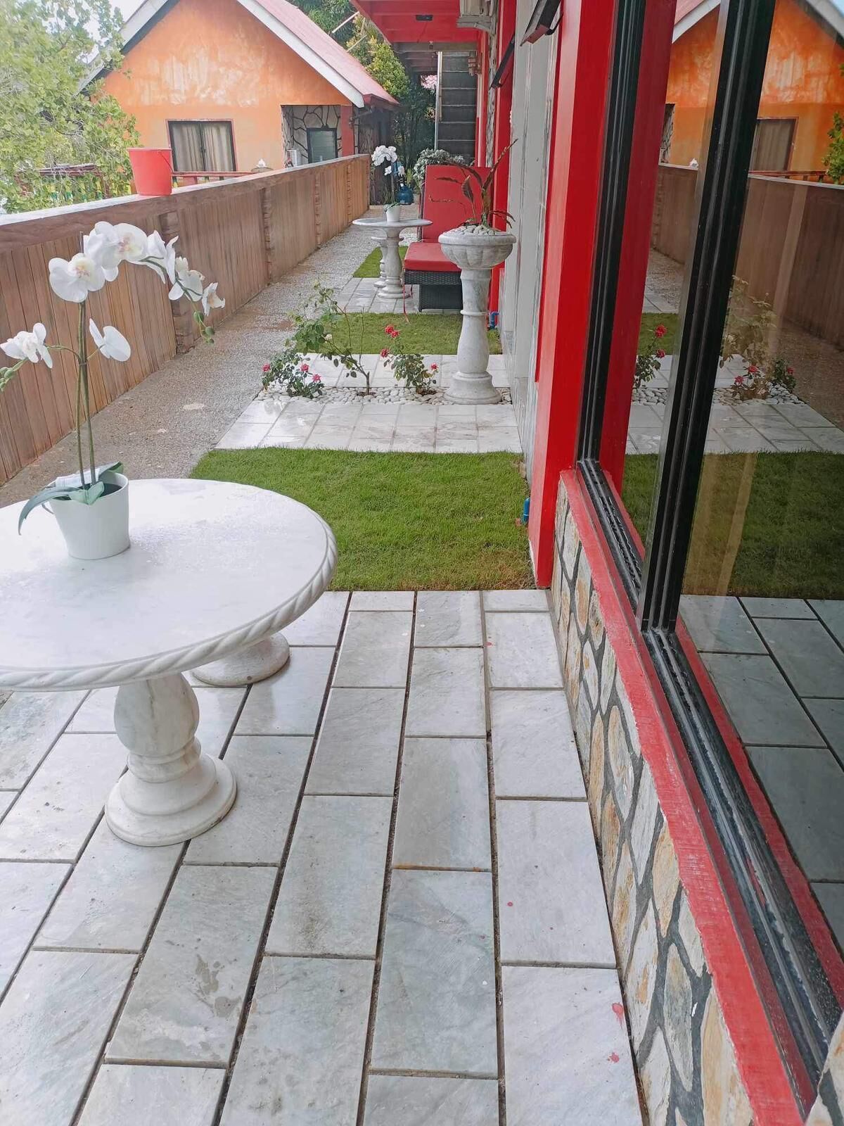 A patio with a white table and chairs, a small lawn, and a red building in the background.