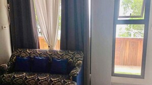 Una habitación con cama, un sofá estampado, una ventana con cortinas y vista a una terraza de madera.