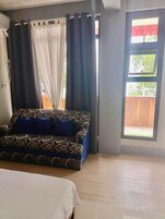 Una habitación con cama, un sofá estampado, una ventana con cortinas y vista a una terraza de madera.