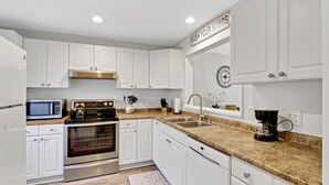 Una cocina moderna con armarios blancos, electrodomésticos de acero inoxidable, una encimera de granito y una cafetera.