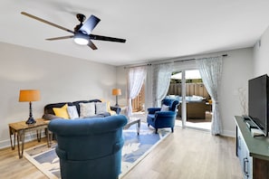 Ein modernes Wohnzimmer mit Deckenventilator, einer Couch, einem blauen Sessel und einem Fernseher.