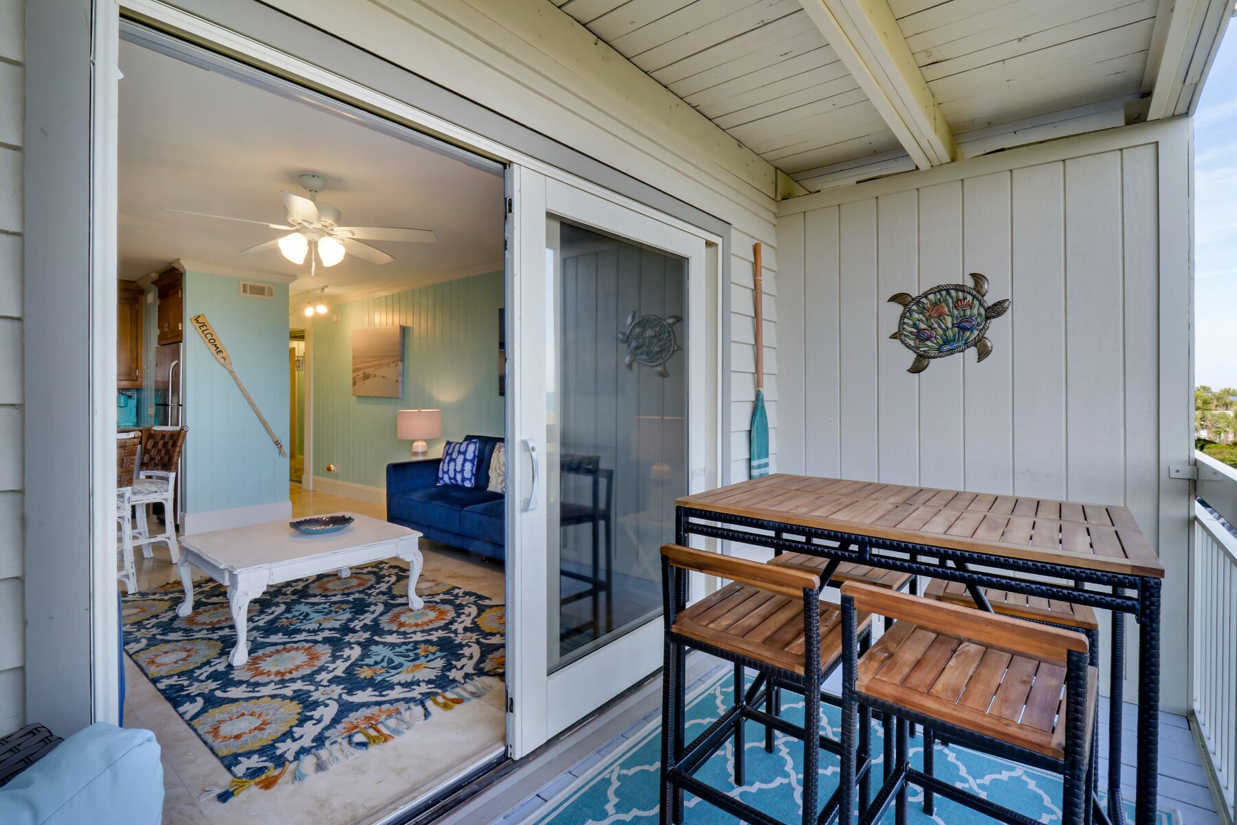 A covered patio with a table and chairs, a blue sofa, a patterned rug, and a welcome sign.
