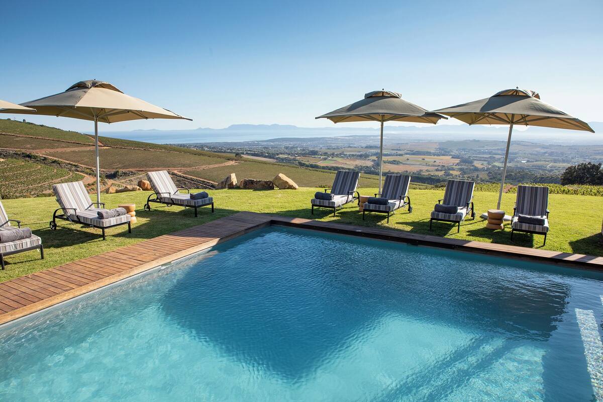 A pool with lounge chairs and umbrellas, overlooking a scenic landscape.