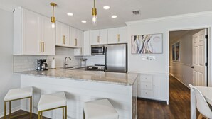 Une cuisine moderne avec des meubles blancs, des appareils en acier inoxydable et un îlot central doté de tabourets de bar.
