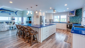 A spacious kitchen with a large island, white cabinetry, and a blue countertop. There are several bar stools around the island and a dining area with a table and chairs. - Rum & Coconuts-You'll be livin' the Caribbean dream! (Hope Town, Bahamas)