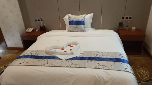 A hotel room with a neatly made bed, a bedside table with a lamp, and a wall socket. - Fangyuan Hotel (Yantai)