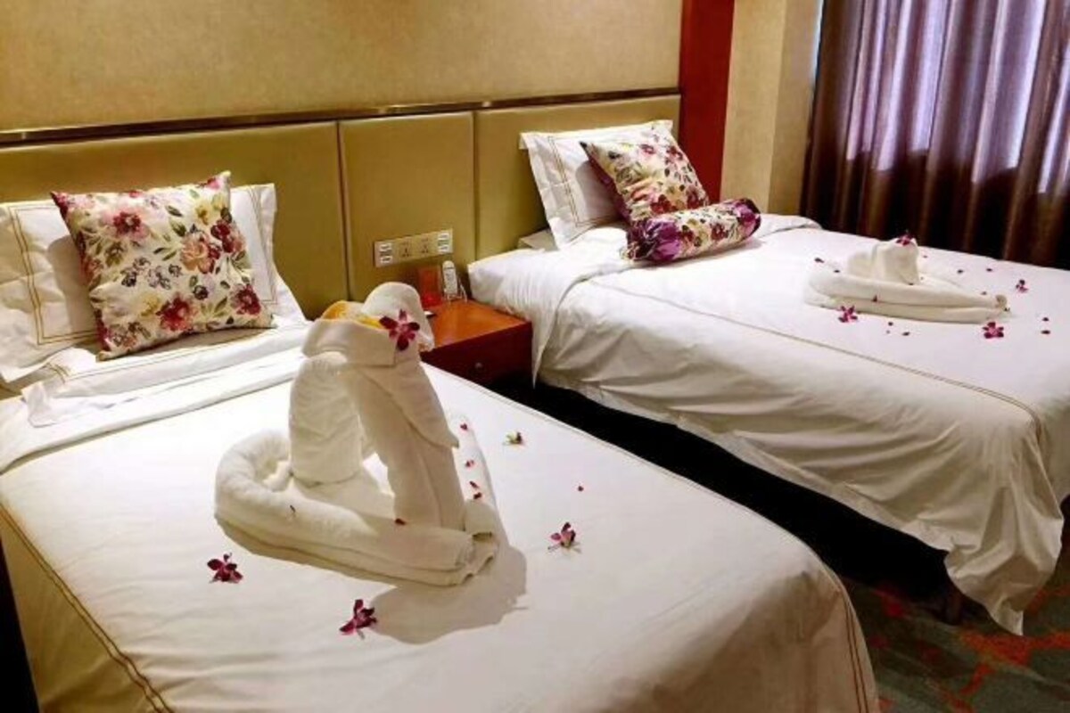 A hotel room with two beds, each with a floral pillow, a nightstand with a phone, and a towel arrangement on one bed.