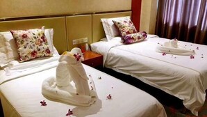 A hotel room with two beds, each with a floral pillow, a nightstand with a phone, and a towel arrangement on one bed. - Fangyuan Hotel (Yantai)