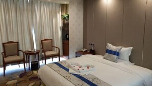 A hotel room with a large bed, two armchairs, a small table, and a nightstand with a phone. - Fangyuan Hotel (Yantai)