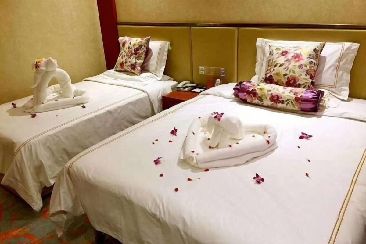 Two hotel beds with towels and flower petals, a telephone, and a nightstand.