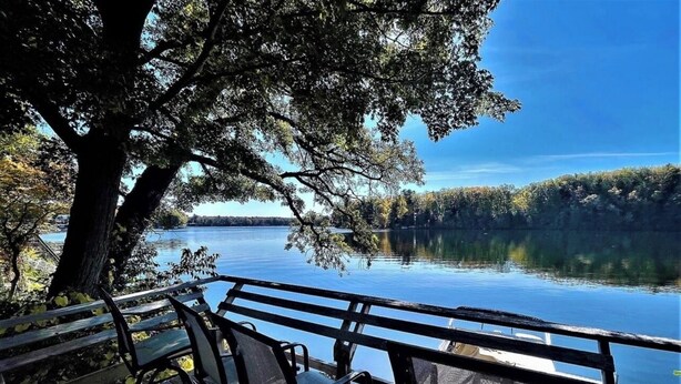 A wooden deck with metal chairs overlooking a calm lake.