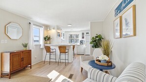 A spacious living room with a striped sofa, a wooden cabinet, and a dining area with wicker chairs.