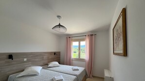 A bedroom with two beds, a window with curtains, a ceiling fan, a framed picture on the wall, and a radiator. - Beautiful T3 for 4/5 people 5 minutes from the beach (Serra-di-Ferro)