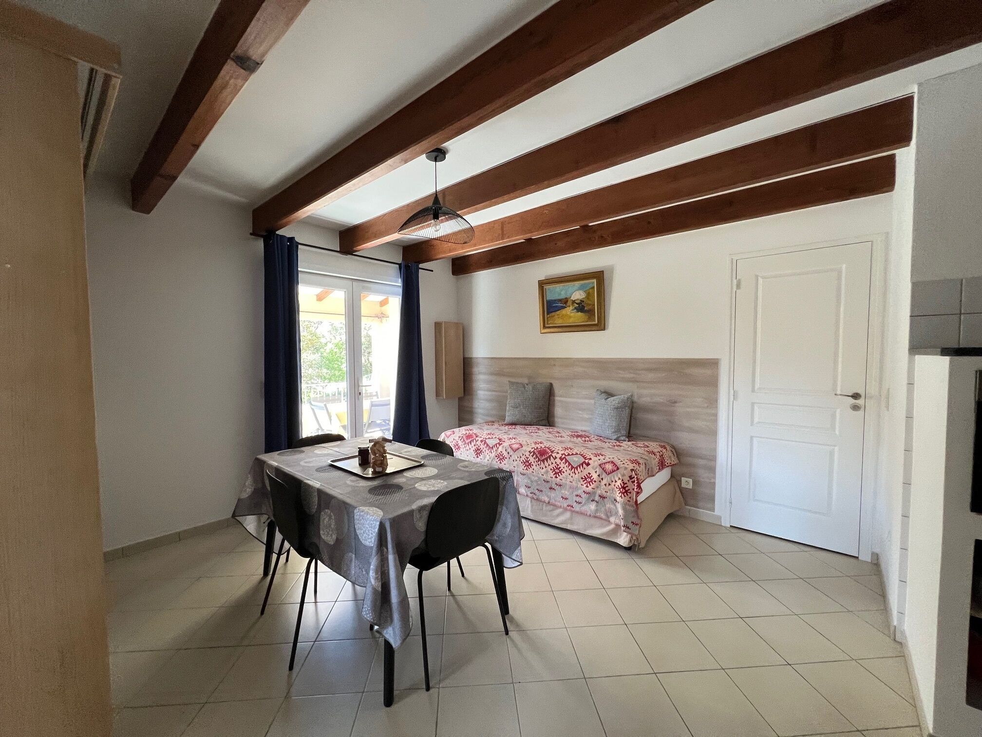 A room with a bed, a table with chairs, a ceiling fan, and a door.