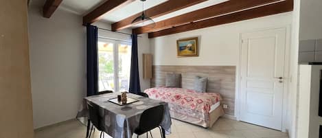 A room with a bed, a table with chairs, a ceiling fan, and a door.