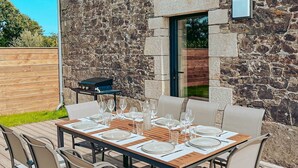 Zona pranzo all'aperto con parete in pietra, una griglia e un tavolo apparecchiato per sei persone.