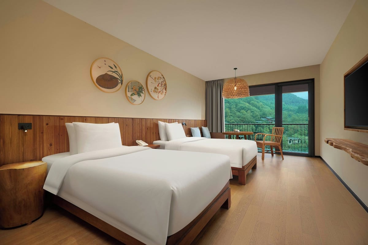 A hotel room with two beds, a balcony with a view, and a wooden floor.