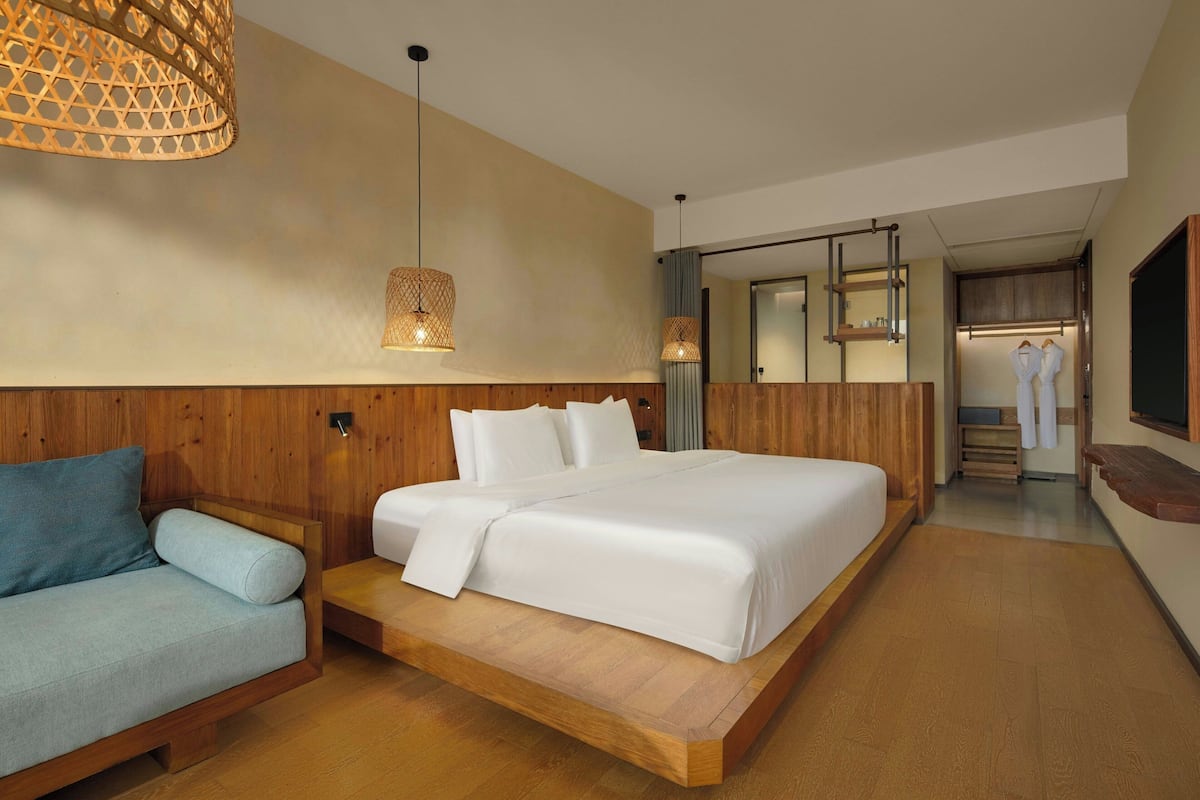 A modern hotel room with a wooden bed, a blue sofa, and a large mirror.