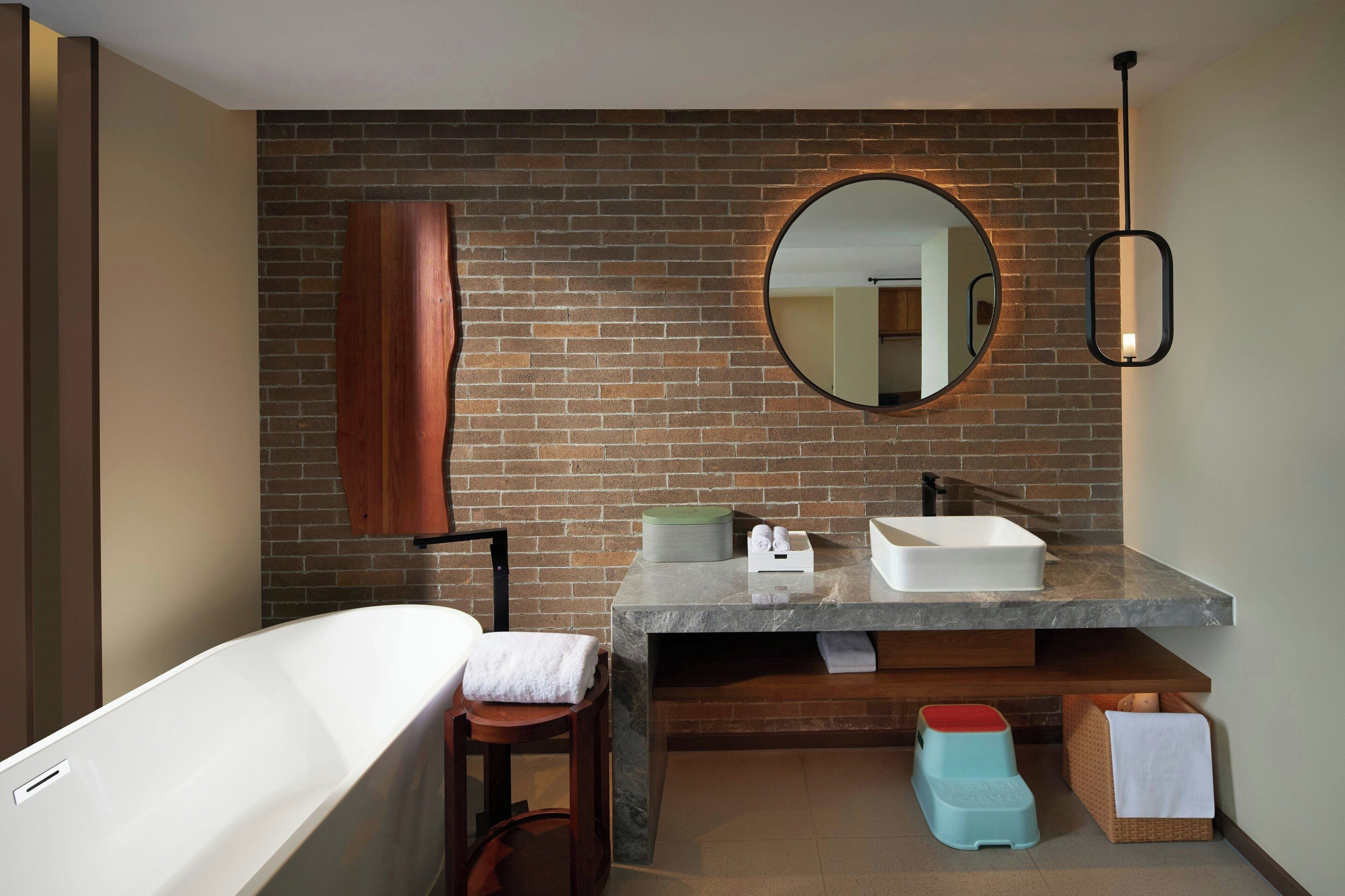 Un baño moderno con pared de ladrillo, una bañera independiente, un espejo grande y encimera de mármol.